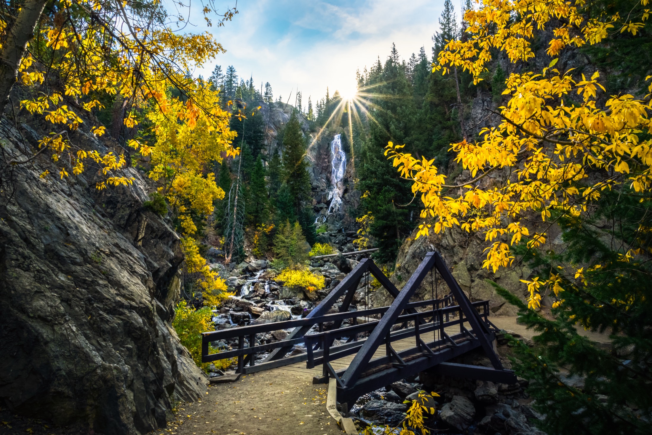 A footbridge before a waterfall framed by golden autumn aspens in the Colorado mountains