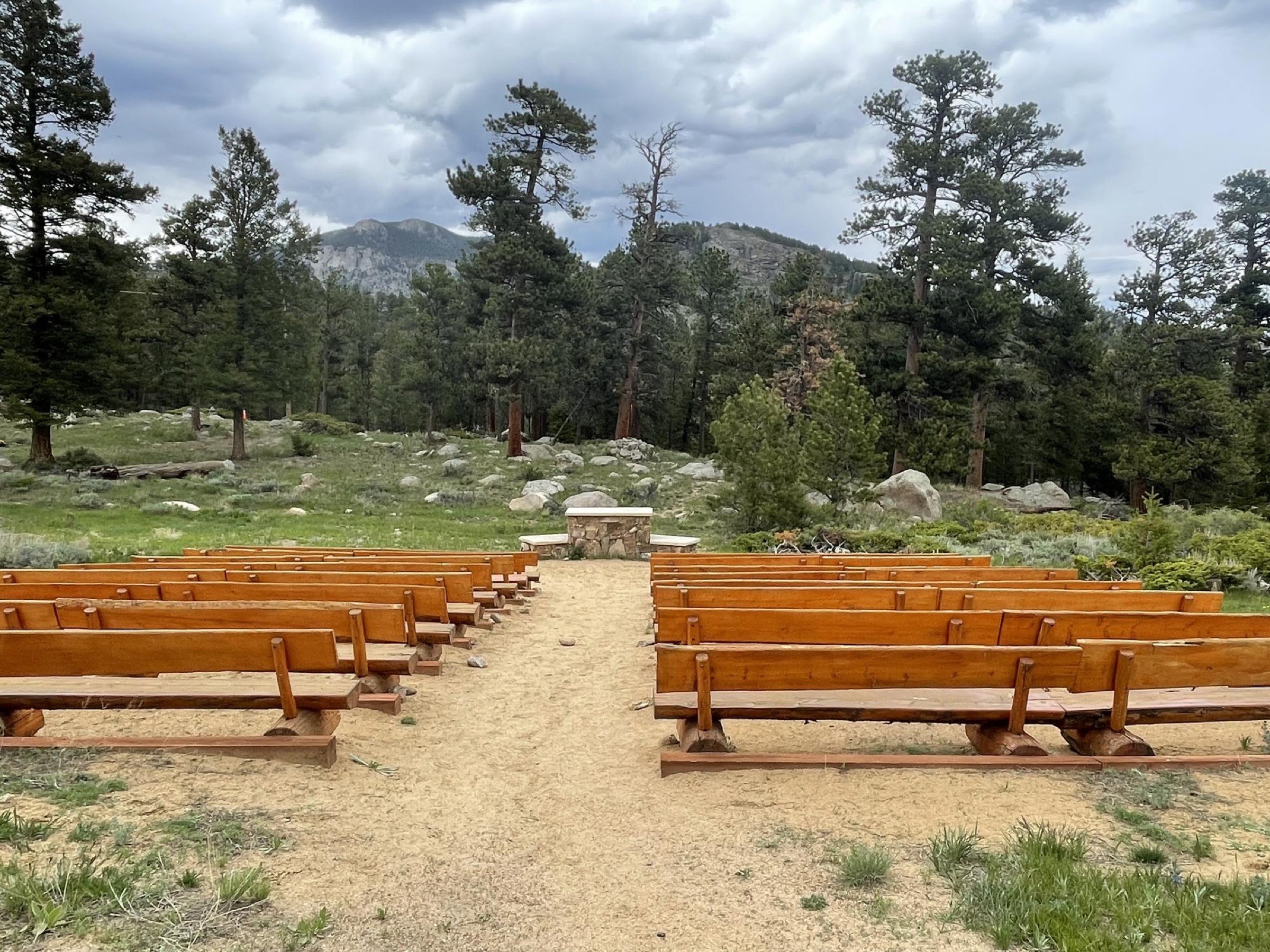 An outdoor mountain sanctuary of wooden pews facing a stone altar at YMCA of the Rockies